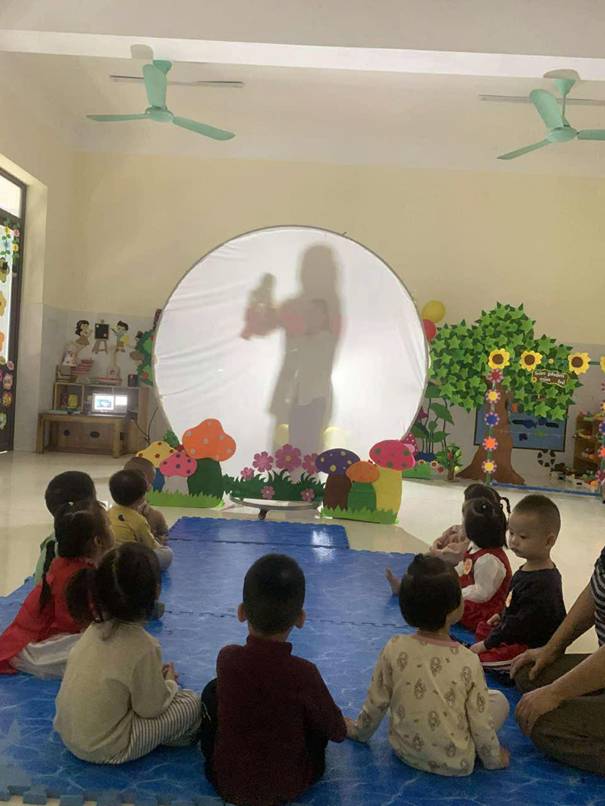 A group of children sitting on a blue mat in front of a white circle with a person in the back

AI-generated content may be incorrect.